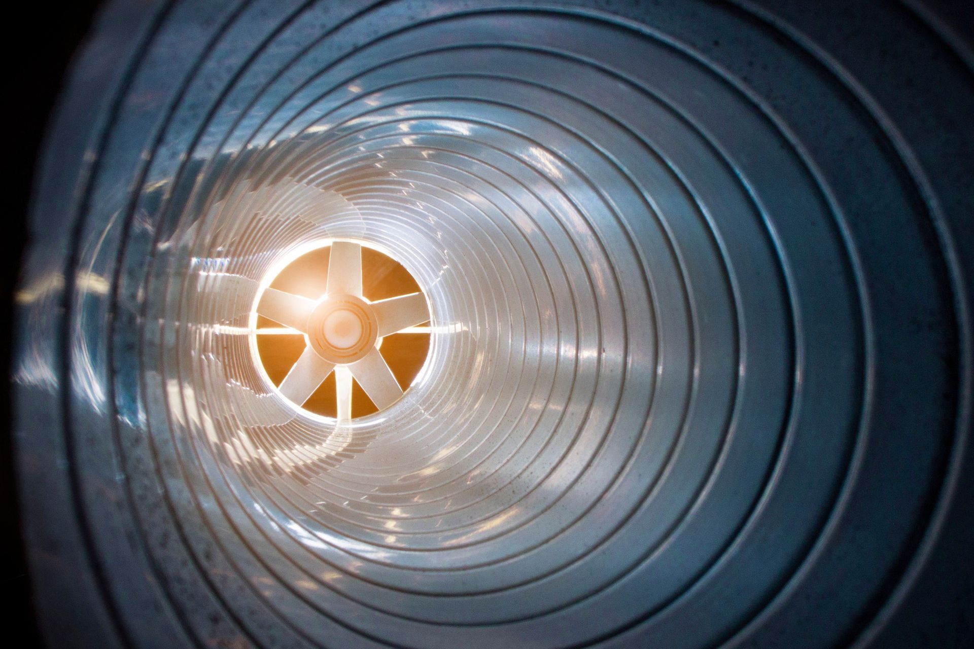 Inside view of a spiral ventilation duct with fan blades at the center, illuminated by warm light. Inside view of a spiral ventilation duct with fan blades at the center, illuminated by warm light.
