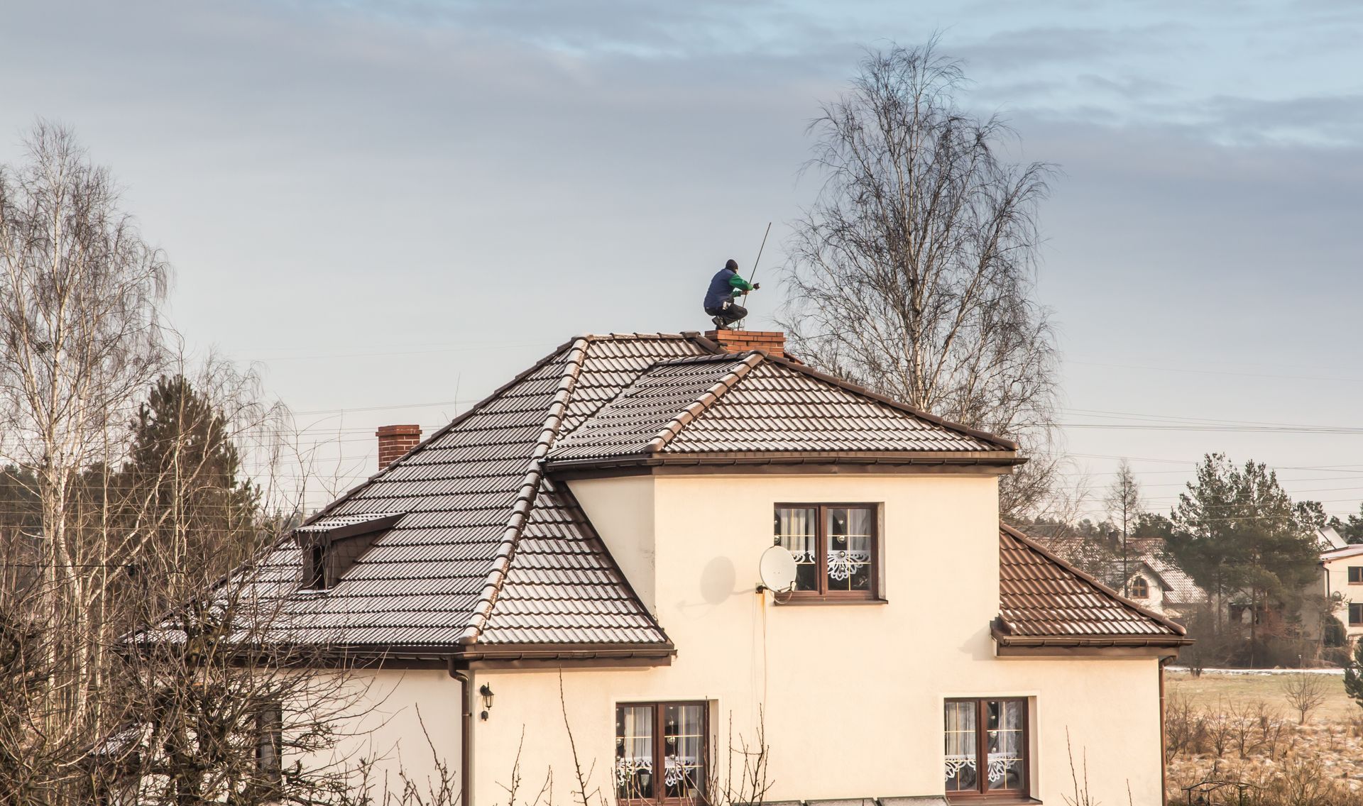 Person on a snowy rooftop of a two-story house, inspecting a chimney. Overcast sky. Person on a snowy rooftop of a two-story house, inspecting a chimney. Overcast sky.