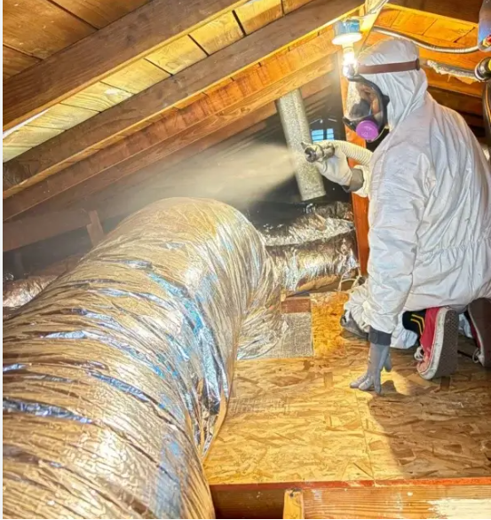 Man in an attic installing ductwork; wearing a hat, gloves, and overalls.