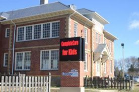 Brick building with sign reading “Community for Kids” and a white picket fence