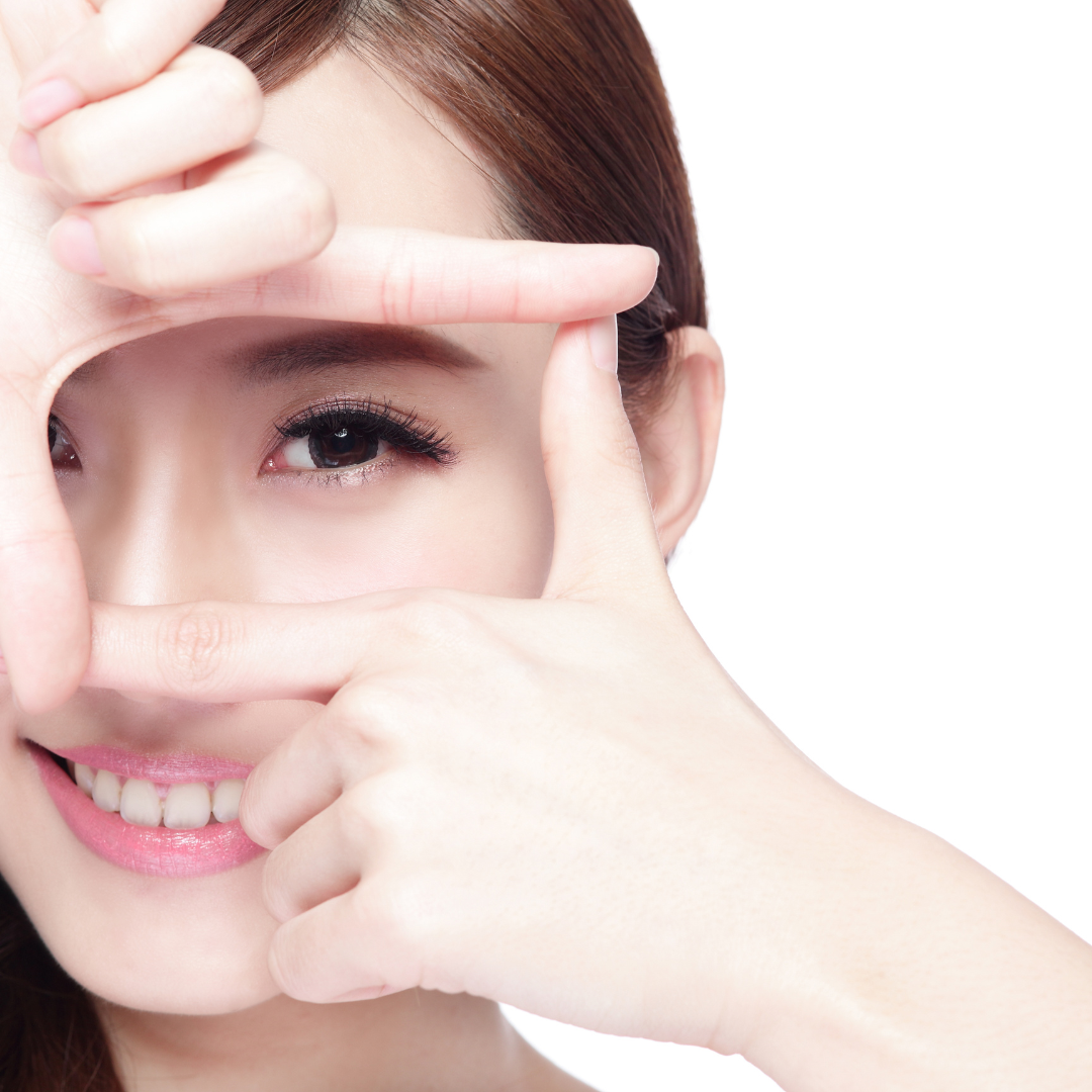 Woman framing her eyes with fingers, smiling.