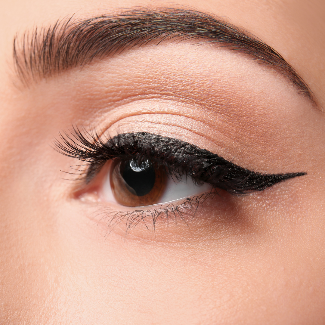 Close-up of a brown eye with dark winged eyeliner and full eyelashes. A groomed eyebrow sits above.