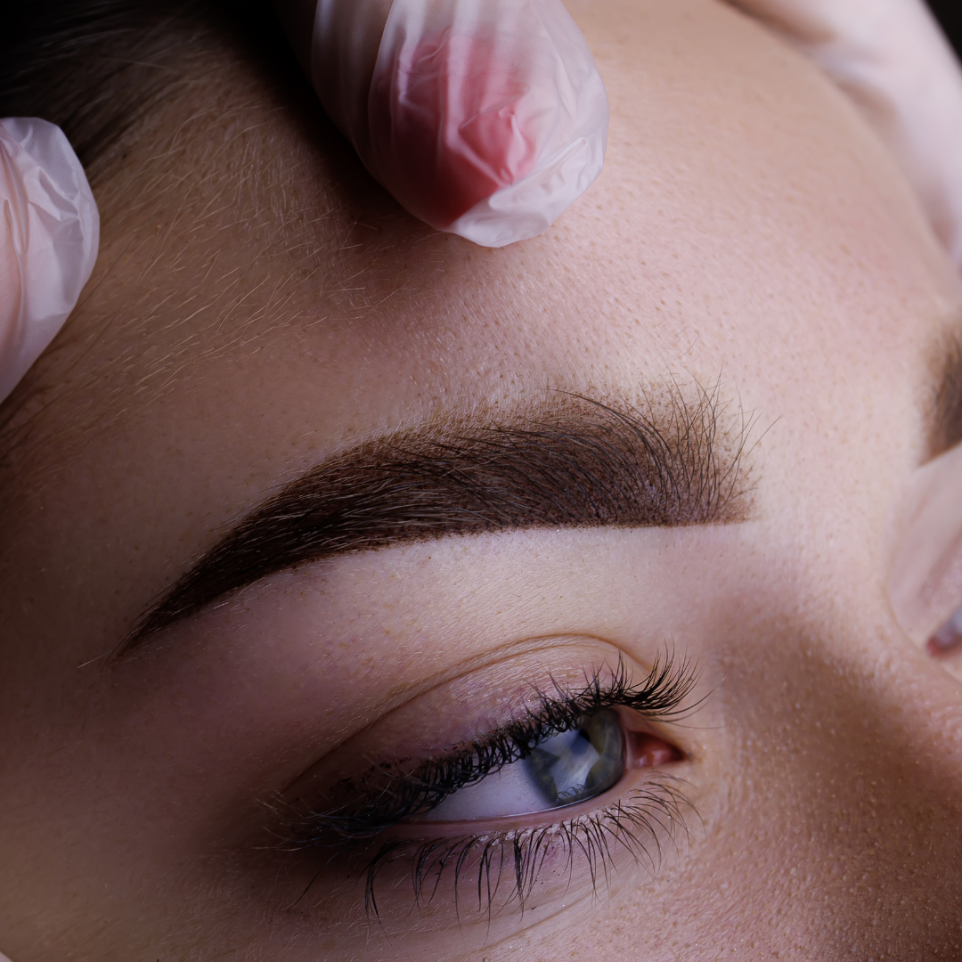 Close-up of a person's eye and eyebrow after a cosmetic procedure, hands in gloves gently touch the eyebrow.