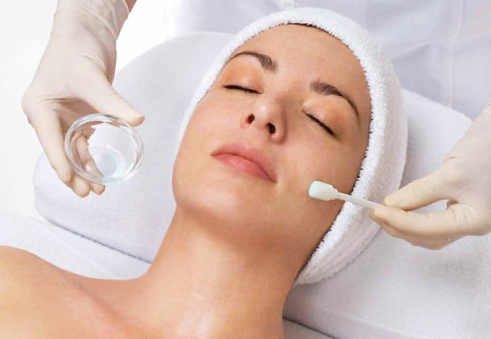 Woman receiving facial treatment, with gloved hands applying product with a cotton swab.