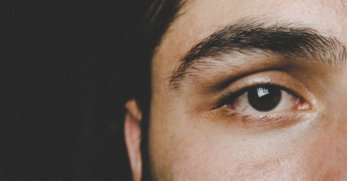 Close-up of a person's eye and eyebrow against a dark background; eye is dark brown.