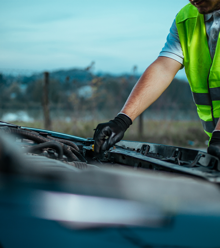 Mechanic in a neon safety vest inspecting a car engine outdoors