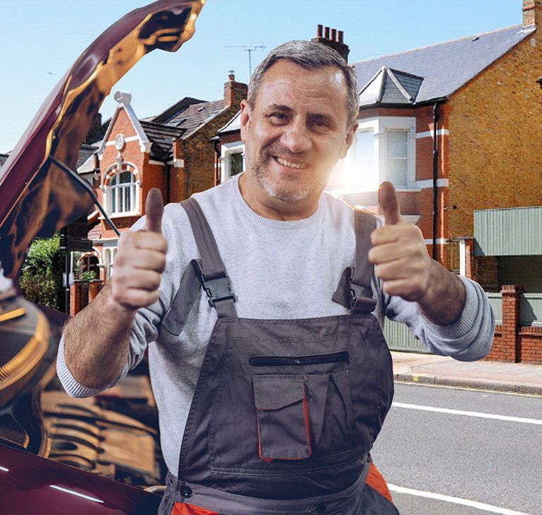Smiling man in gray overalls gives two thumbs up on a sunny street, with houses and a backhoe behind him