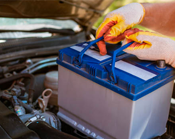 Hands in gloves inspecting a car battery under the open hood