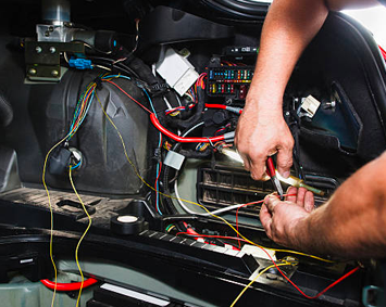 Technician wiring and repairing the inside of a car dashboard area with exposed cables and tools