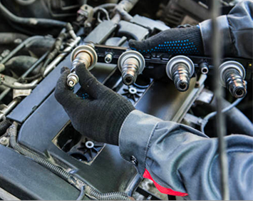 Gloved mechanic tightening spark plugs on an engine with four ignition coils