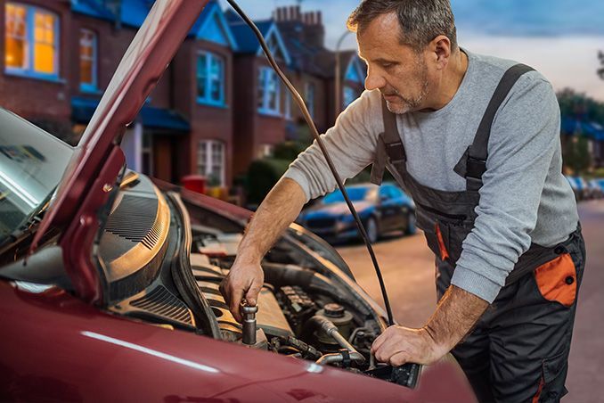 Mechanic inspecting a maroon car engine with the hood open on a residential street