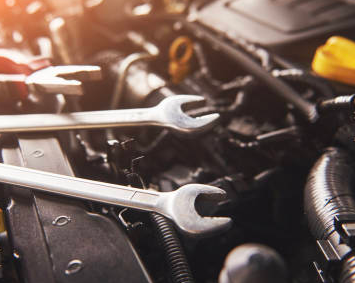 Two silver wrenches resting on a car engine in a garage, with warm light shining over black components