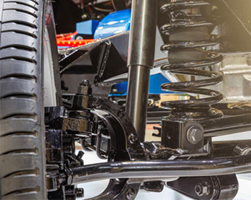 Close-up of a vehicle’s rear suspension, tire, and coil spring with black mechanical parts.