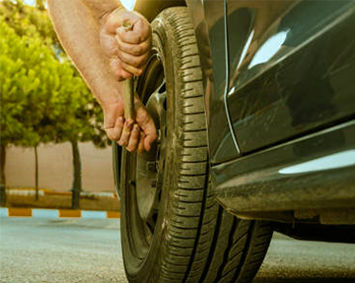 Person changing a car tire outdoors on a sunny street