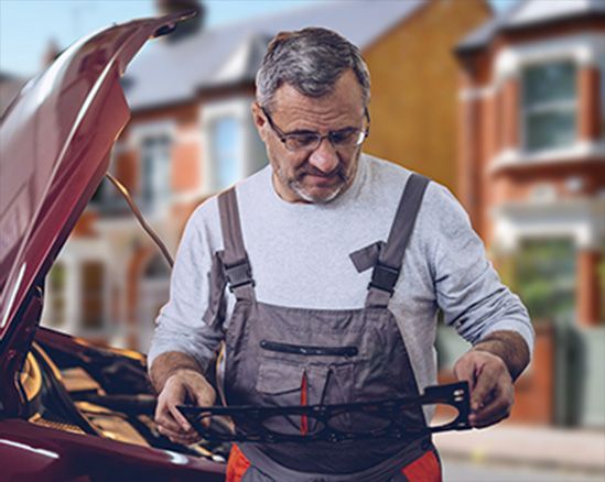 Mechanic in gray overalls checking a car engine with the hood open
