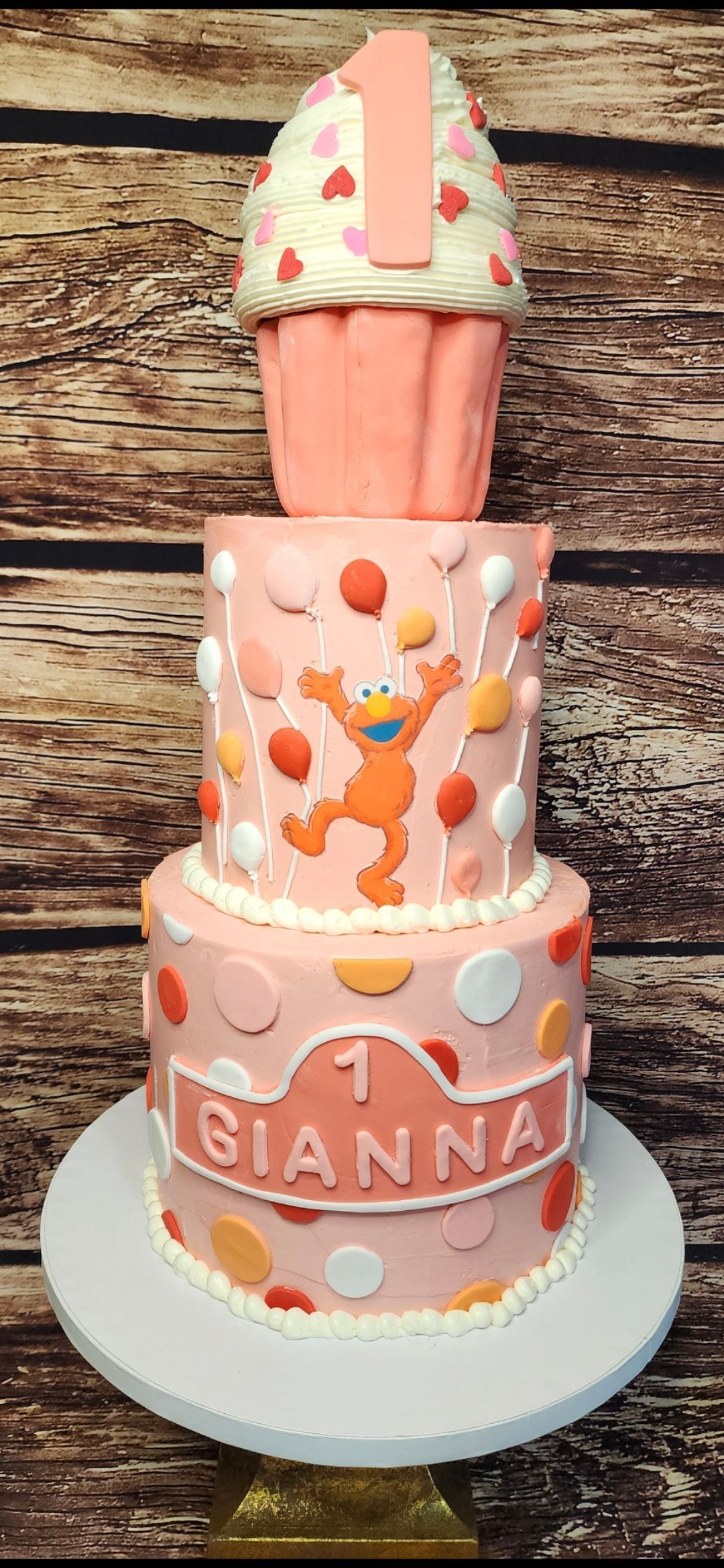 A pink cake with a cupcake on top of it for a girl 's first birthday.