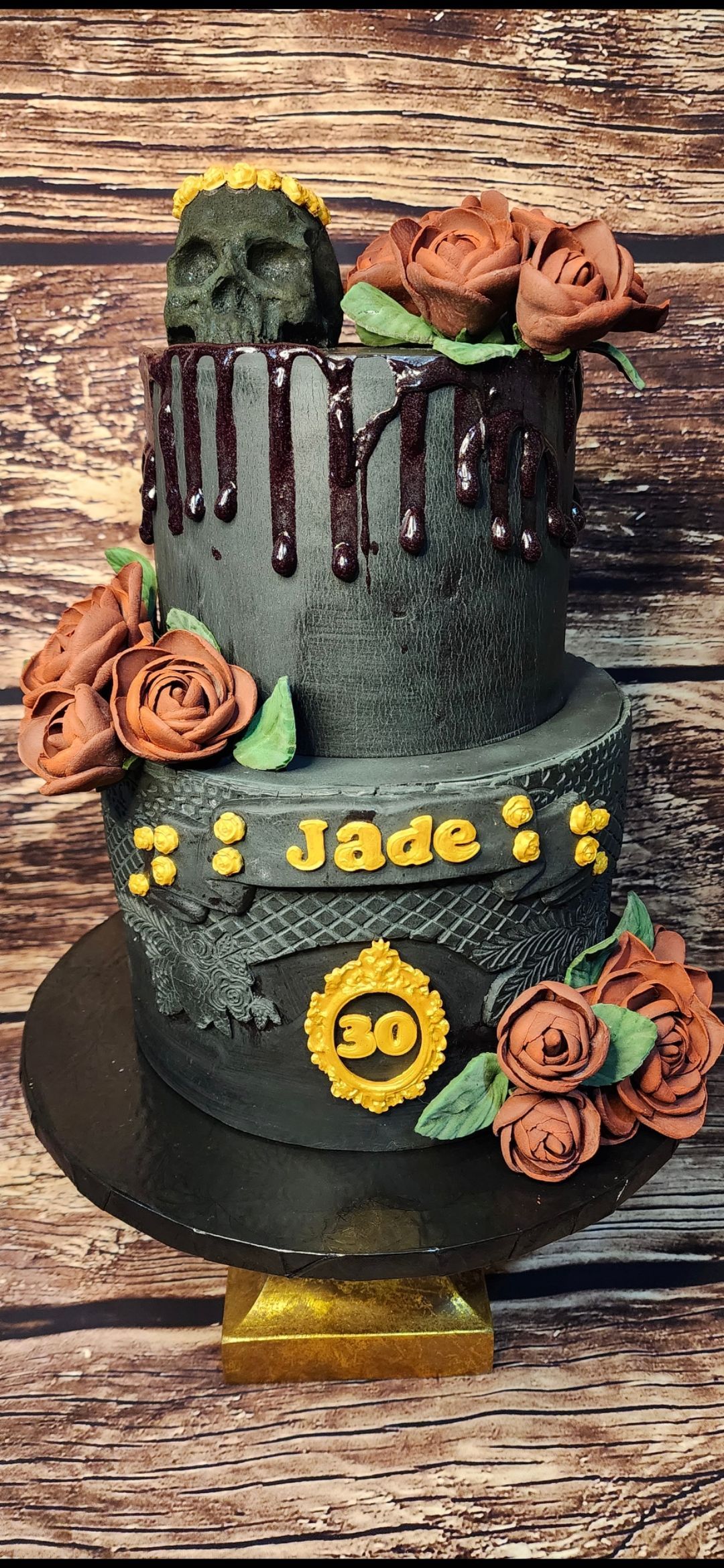 A black cake with roses and skulls on it is on a wooden table.