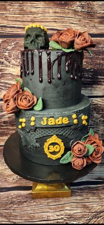 A black cake with roses and skulls on it is on a wooden table.