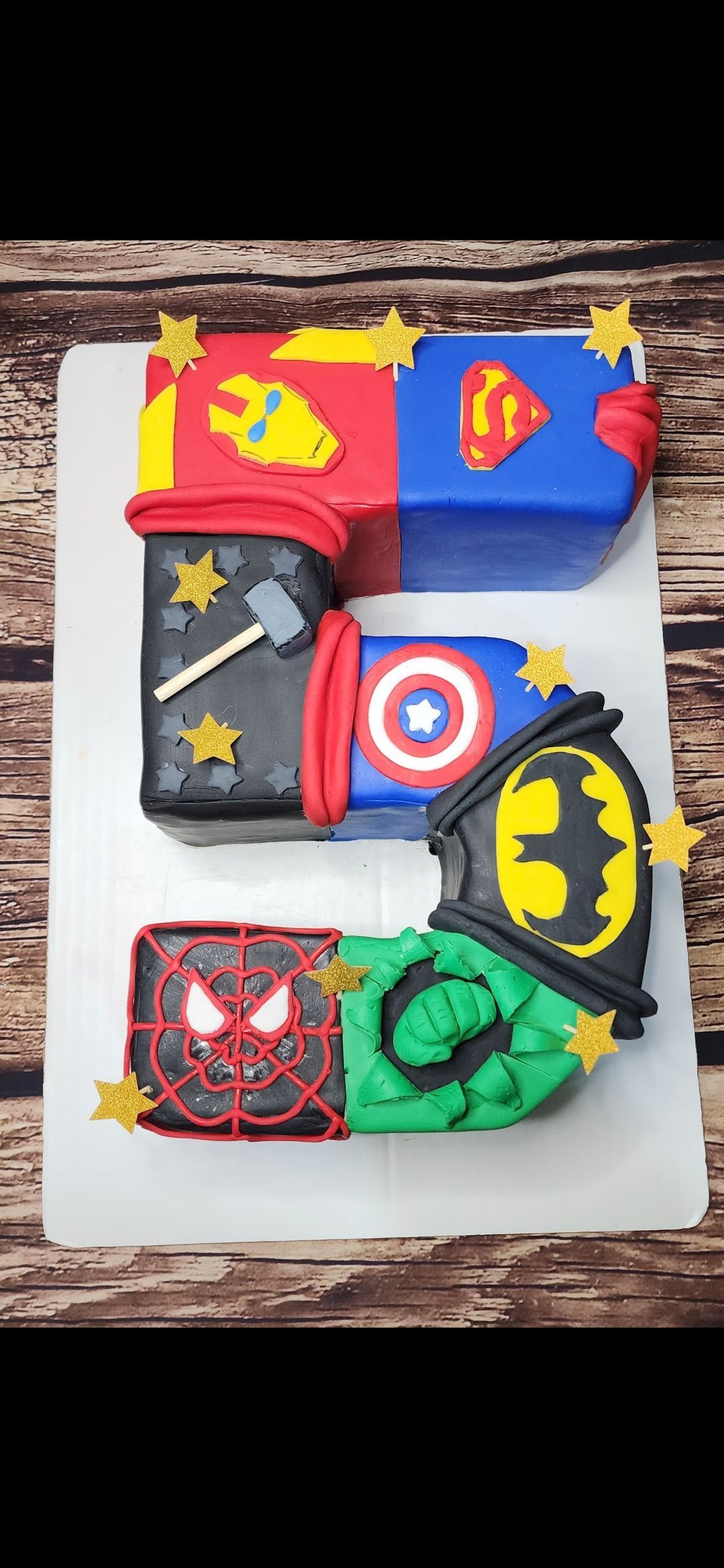 A cake in the shape of the number 5 with superhero logos on it.