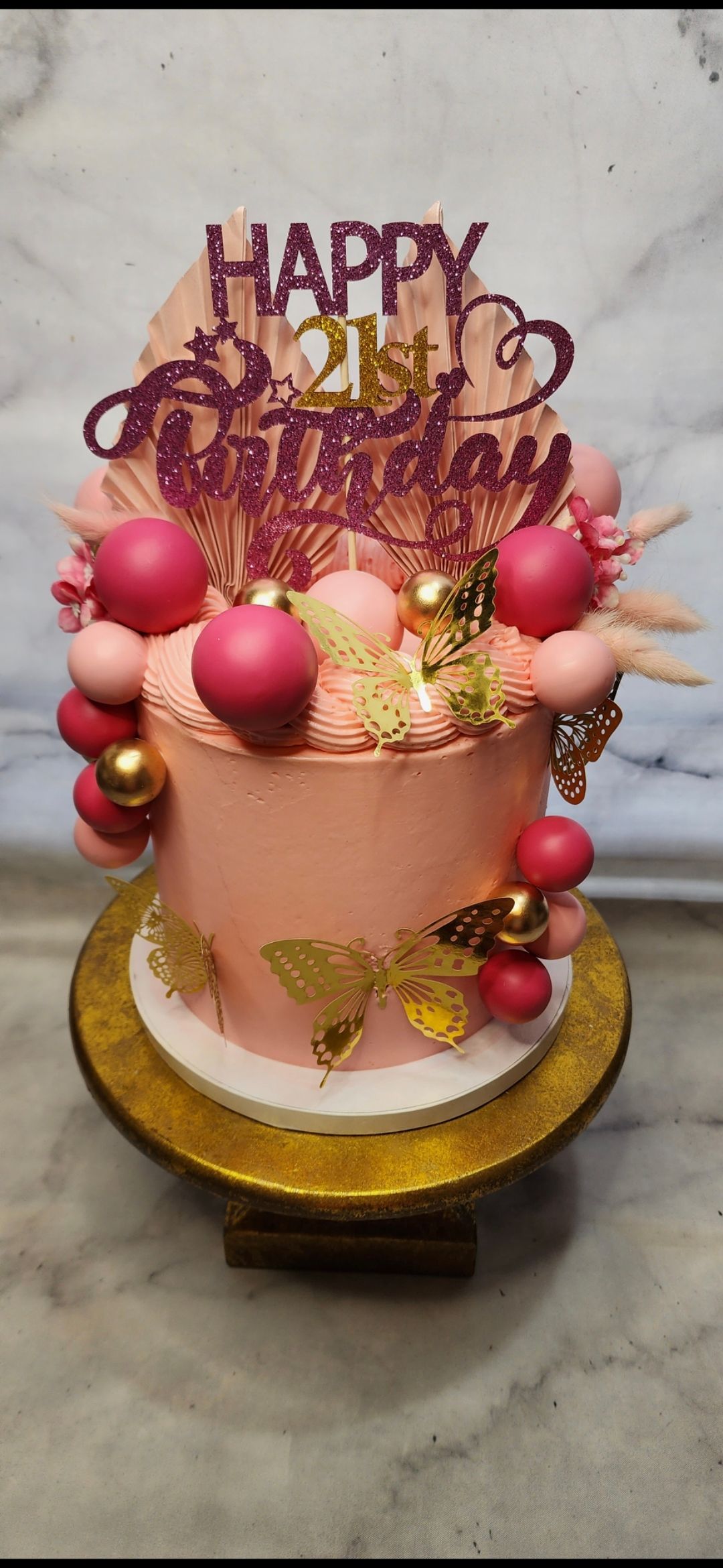 A pink birthday cake is sitting on top of a gold cake stand.