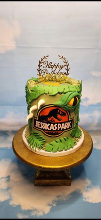 A cake with a dinosaur on it is on a cake stand.