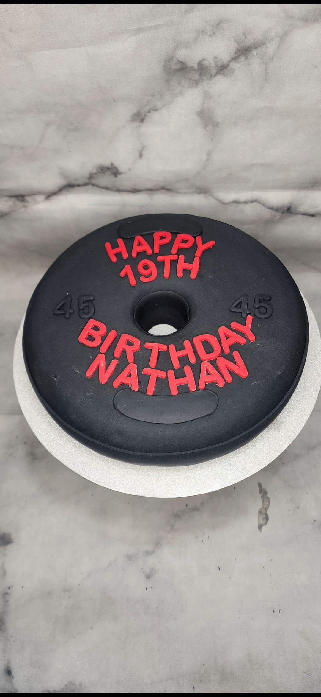 A black donut cake with the words `` happy 19th birthday nathan '' written on it.