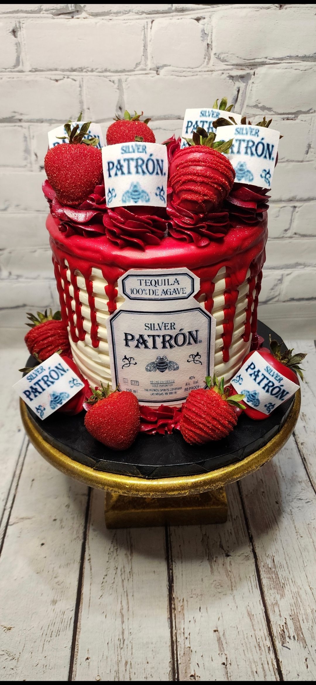 A cake with strawberries and patron bottles on top of it.