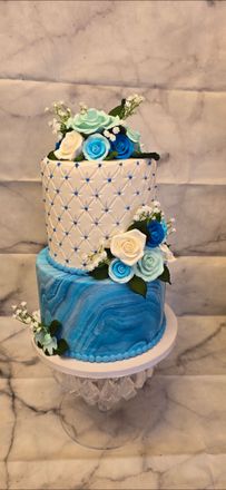A blue and white cake with flowers on top is sitting on a marble table.