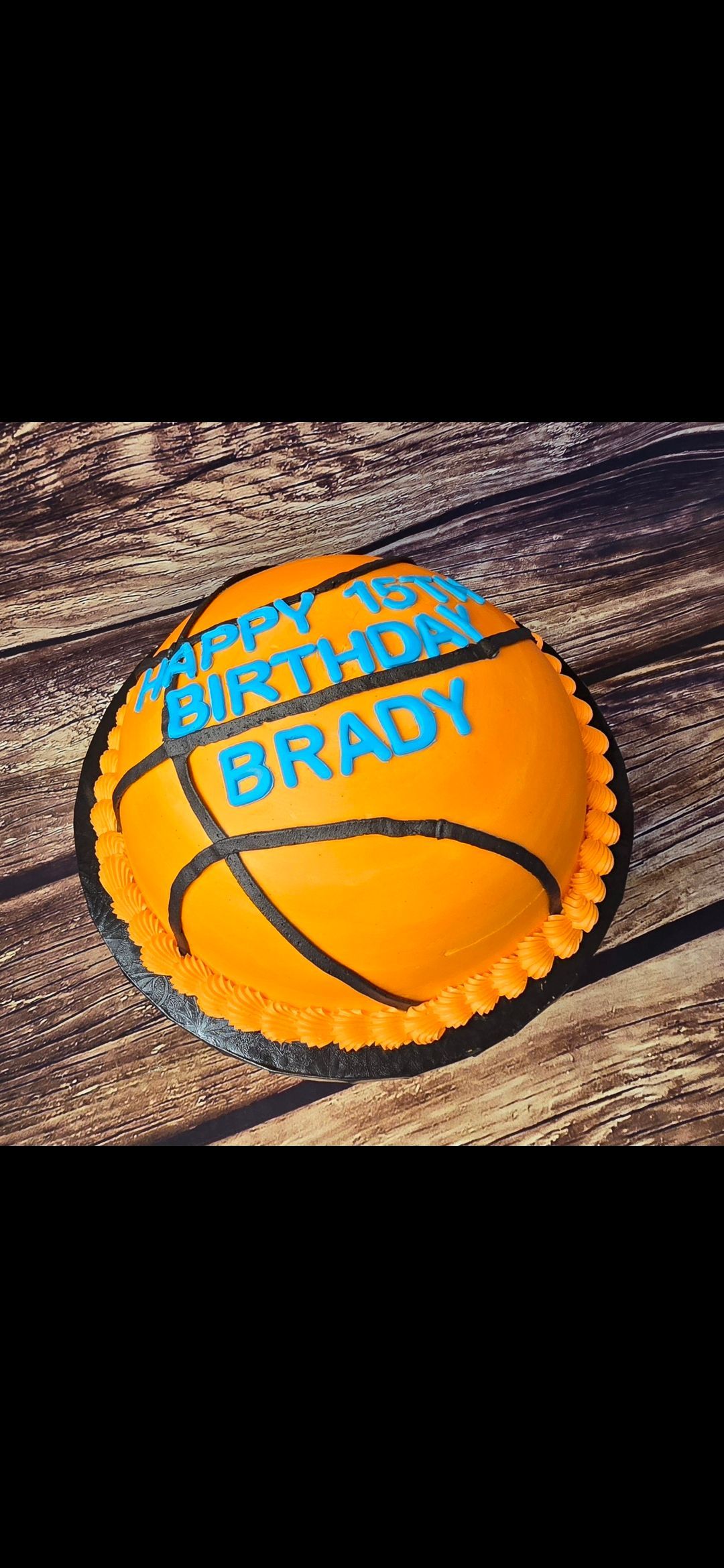 A birthday cake in the shape of a basketball is sitting on a wooden table.