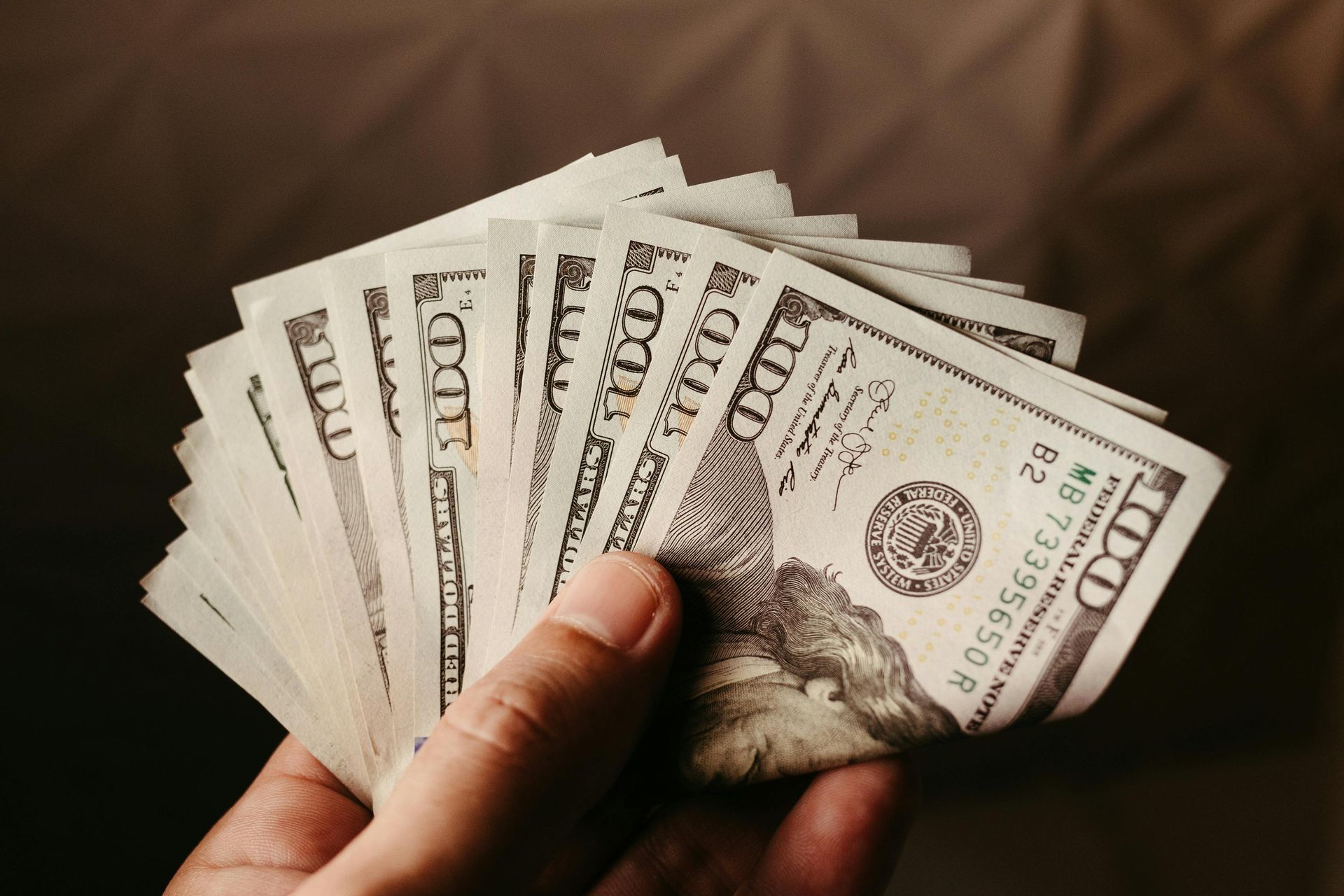 Hand holding a fan of U.S. dollar bills against a brown patterned background