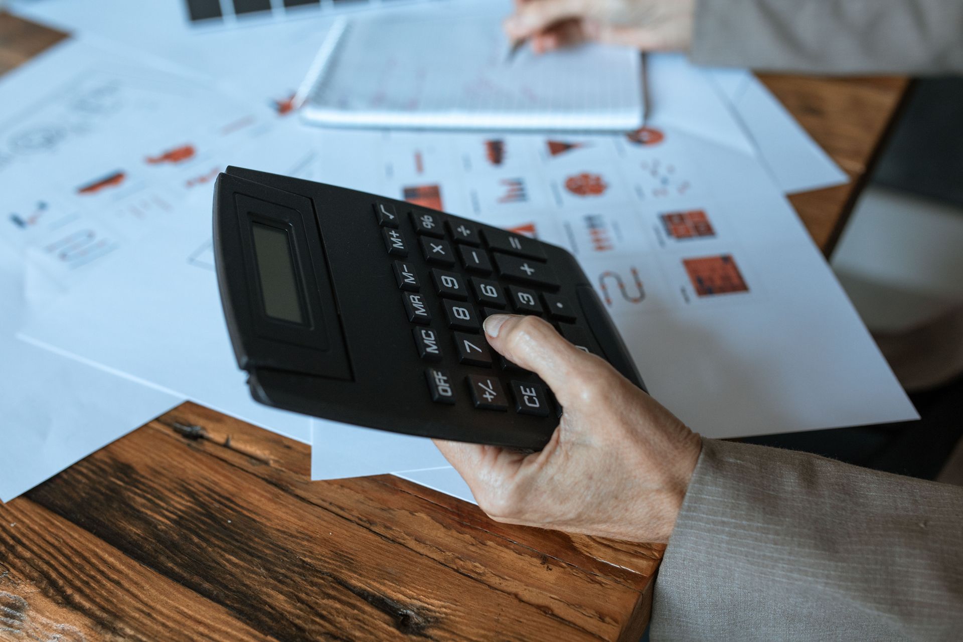Hand holding a black credit card terminal over paperwork on a wooden desk