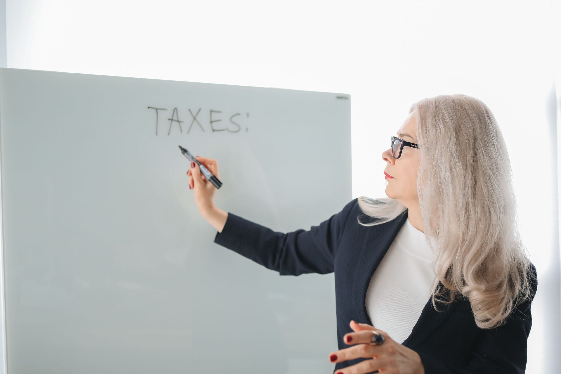 Woman writing “TAXES” on a whiteboard in a bright office