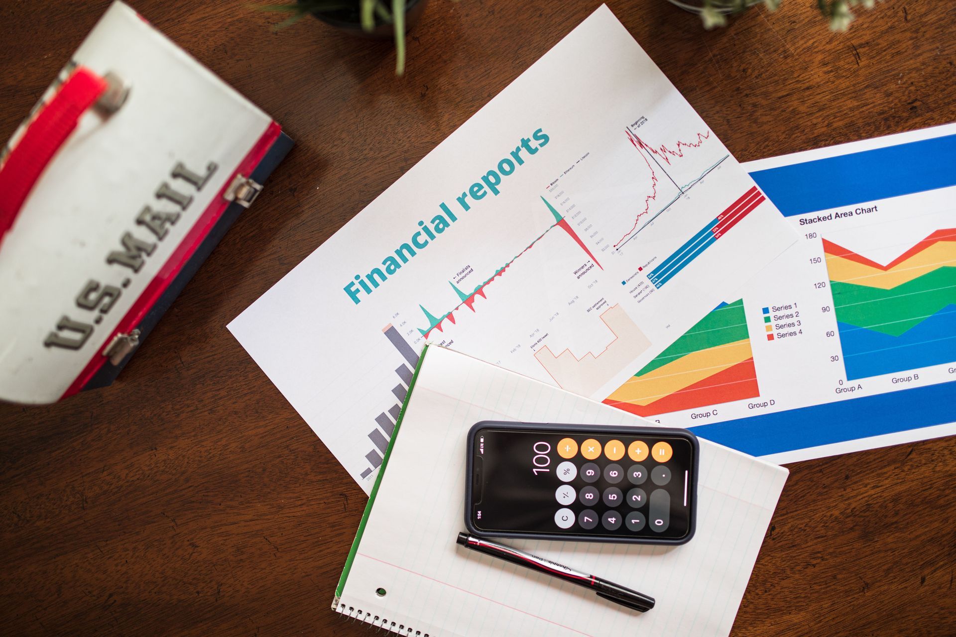 Financial reports on a desk with charts, calculator, pen, and a U.S. mail envelope
