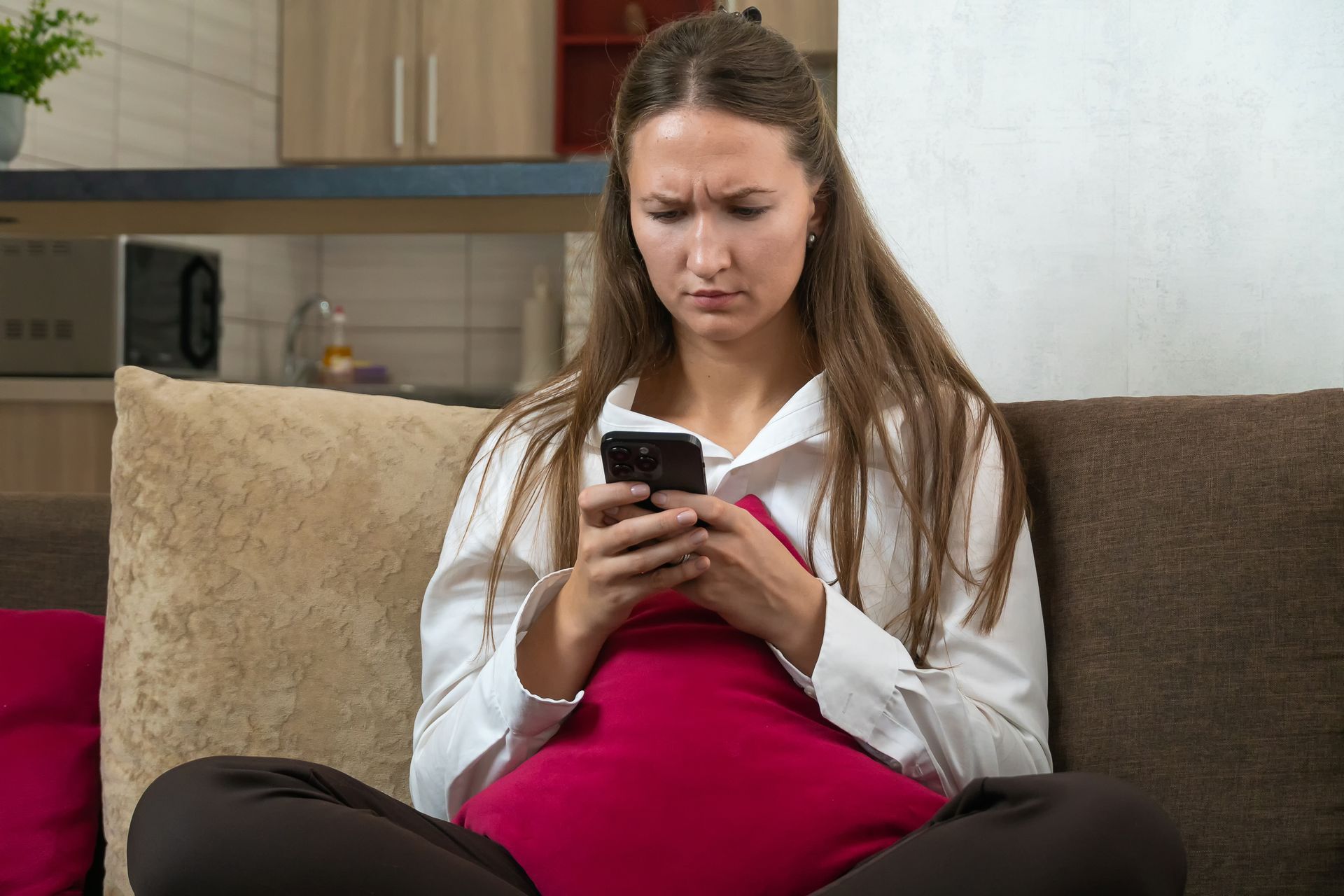 Woman with a concerned expression on her face looking at her phone while sitting on a couch.