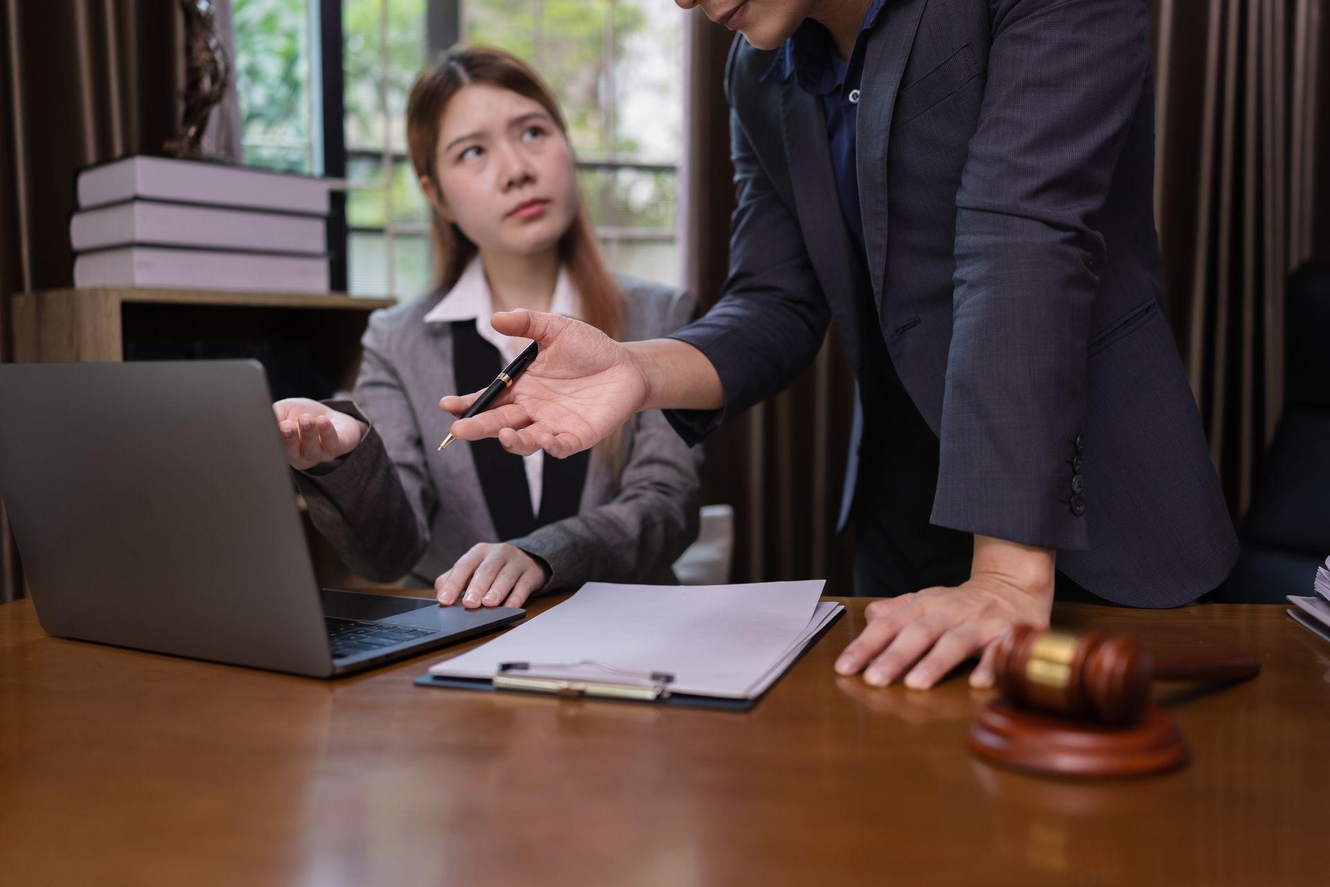 Woman at laptop and man pointing at document, in office with gavel.