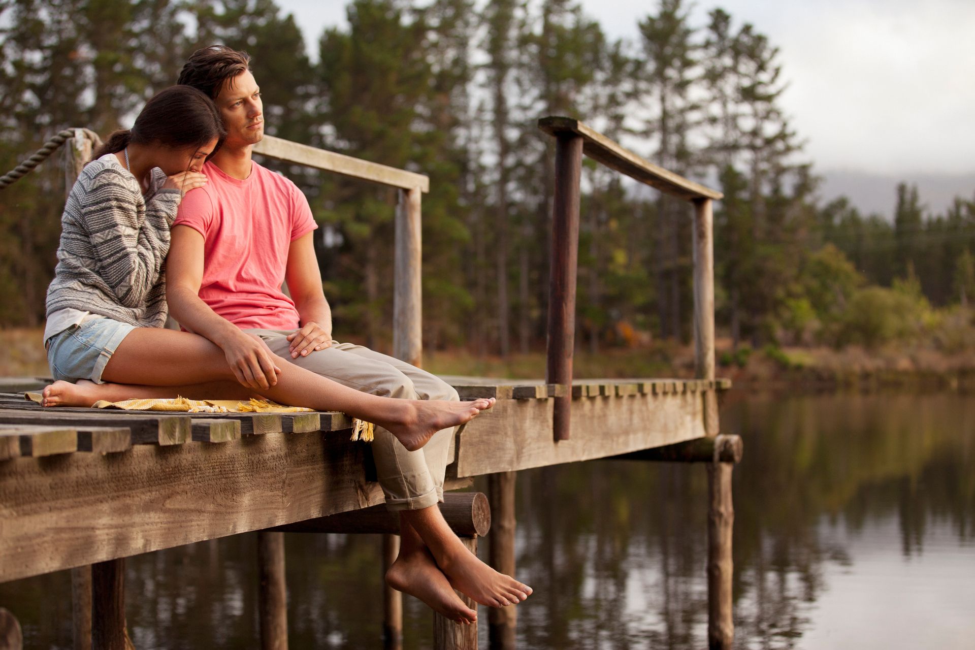 Couple sitting on a wooden dock by a calm lake, enjoying the peaceful outdoor scenery.
