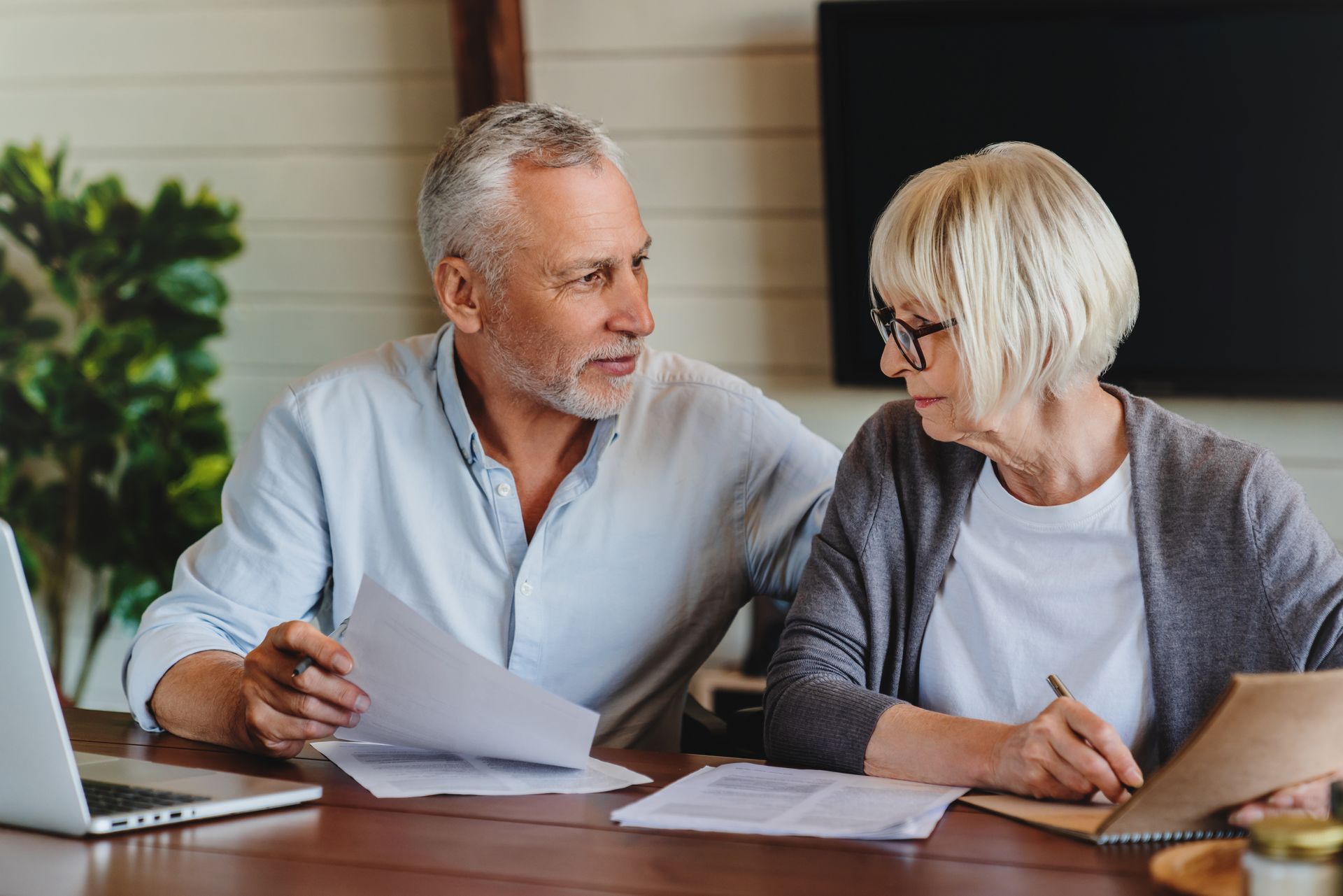 Senior couple reviewing documents together at a table, discussing finances.