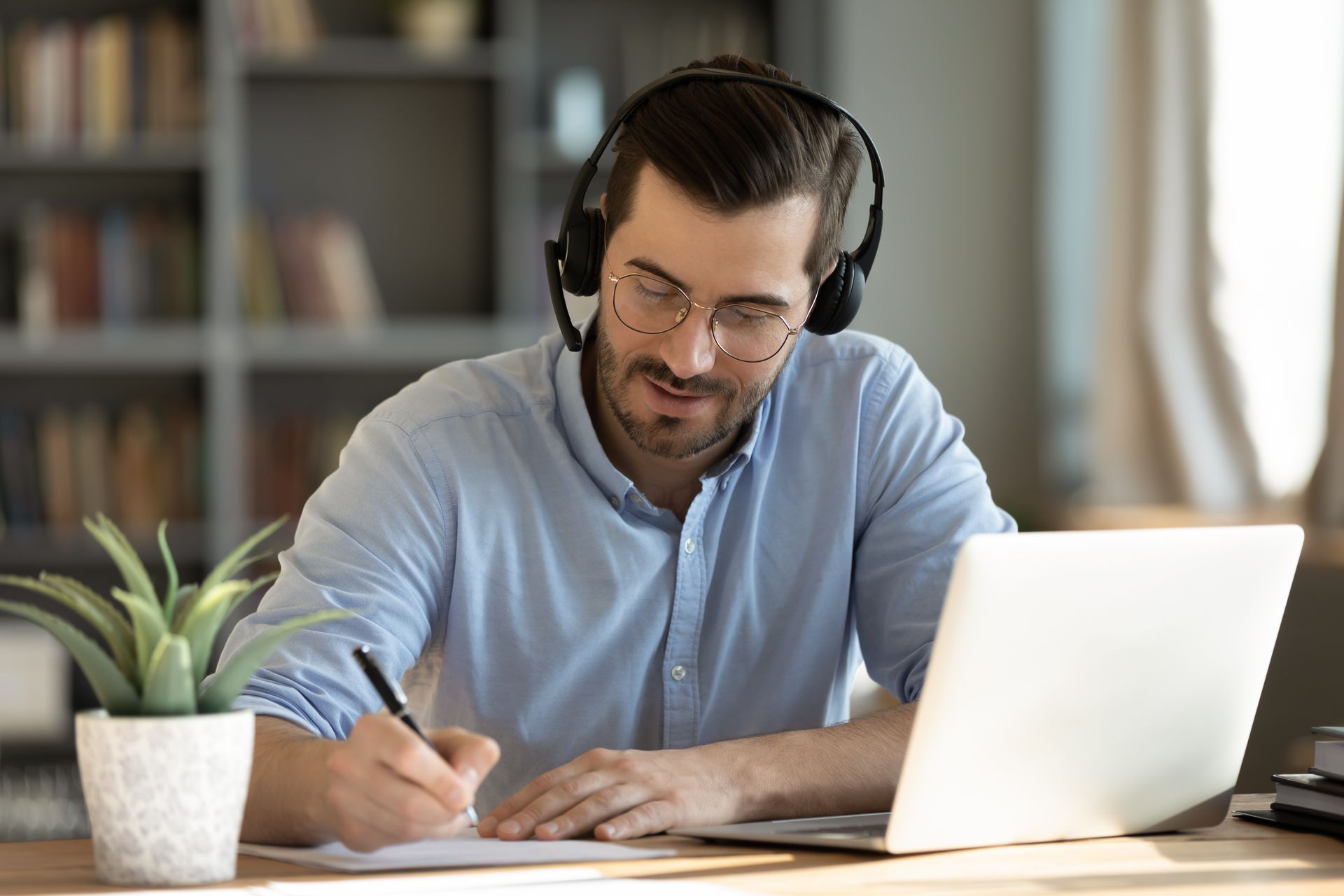 A man wearing headphones is sitting at a desk using a laptop computer.