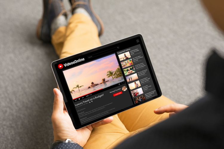 Person holding a tablet, watching a YouTube video with tropical beach scene, sitting.