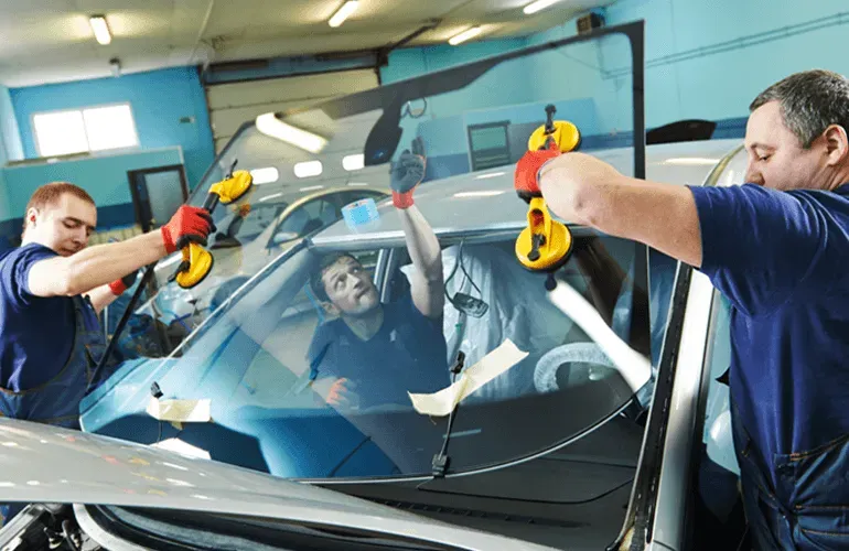 Technicians using suction cups to remove a windshield from a car in a workshop