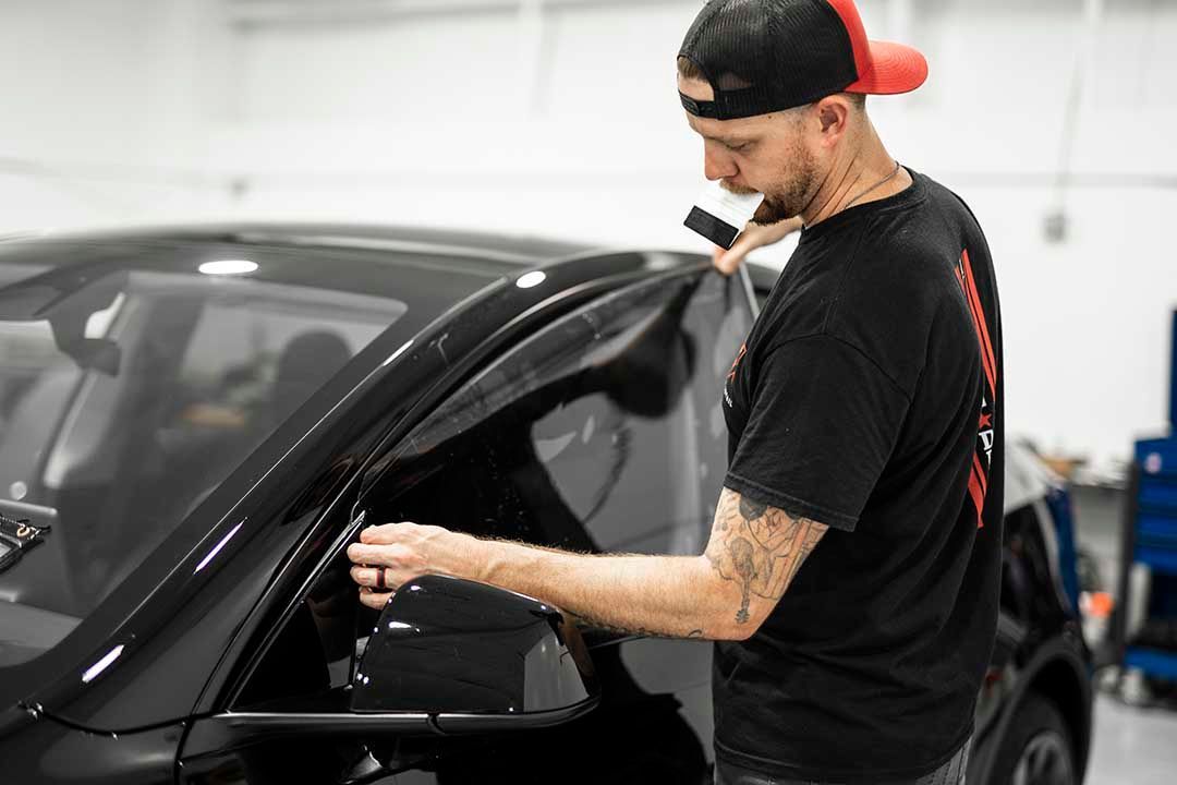 Man in a black shirt working on a black car window in a garage