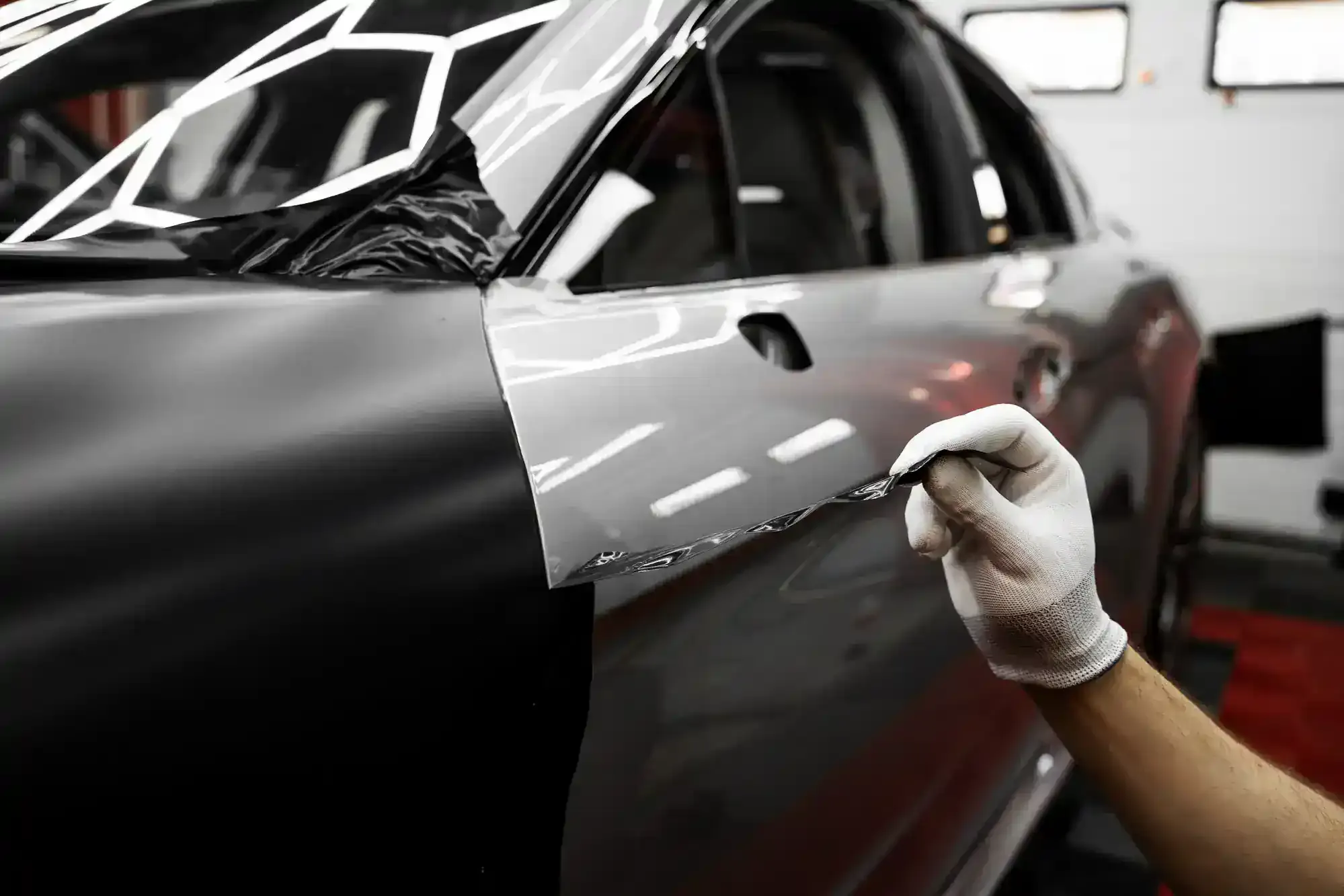 Person applying gray wrap film to a black car door in a workshop