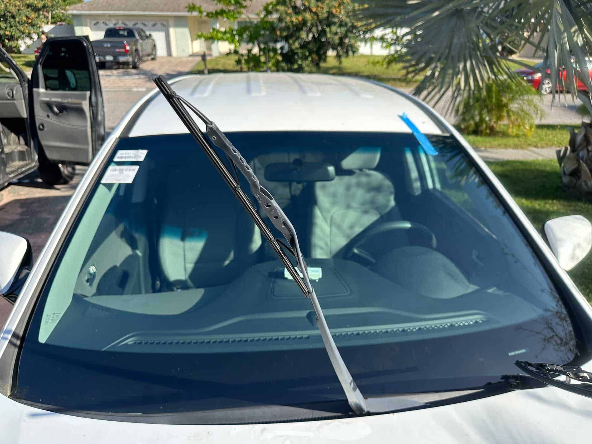 Black car windshield with a wiper blade raised, parked outdoors in a driveway.