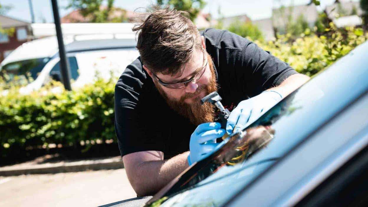 Technician in blue gloves repairing a car windshield outdoors with tools