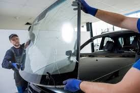 Two workers in gloves install a large windshield onto a car in a garage.