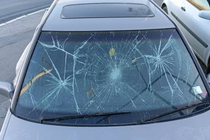 Gloved hands repairing a car windshield near the edge of the glass