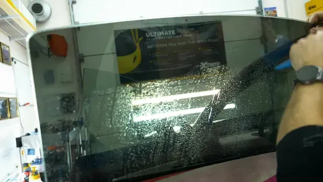 Shattered car windshield with spiderweb cracks, person’s arm visible on the right in a workshop.