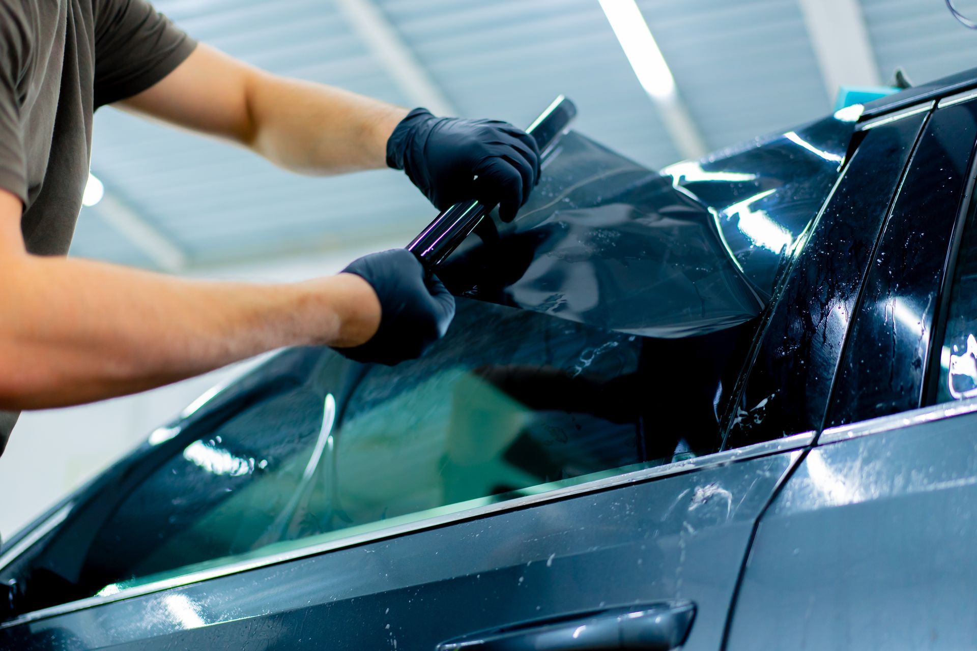 Worker applying window tint to a car windshield in a garage
