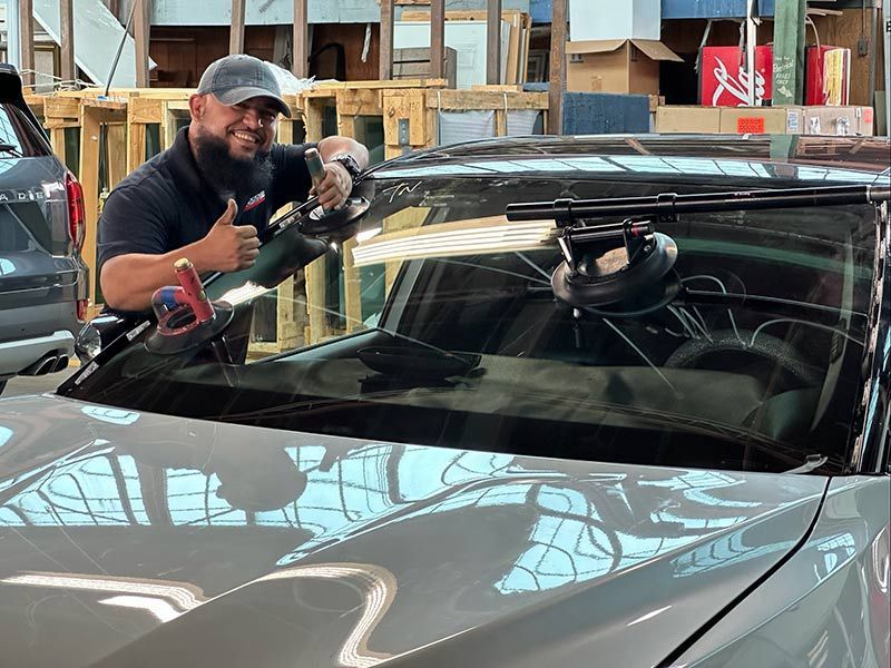 Man using a suction cup tool to install a windshield on a black car in a workshop