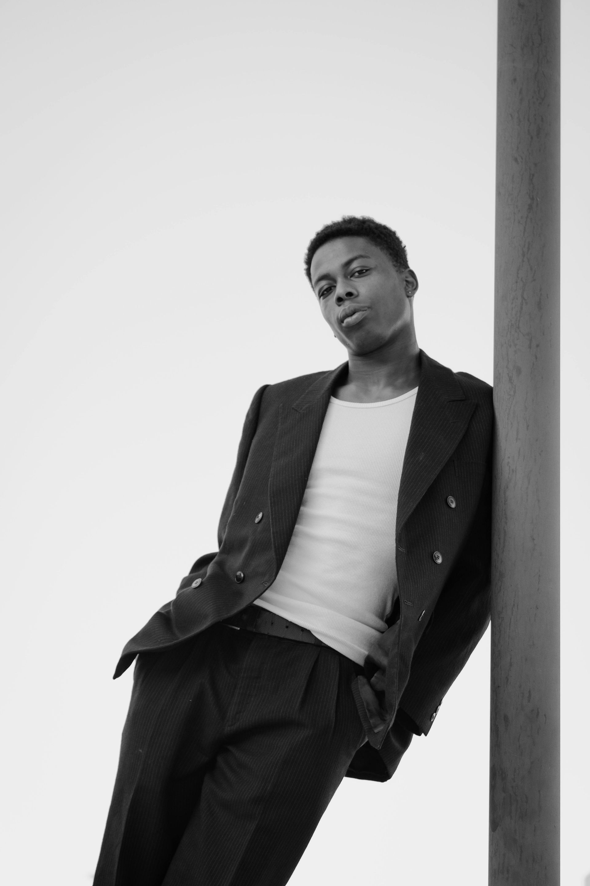 A black and white photo of a man leaning against a pole.